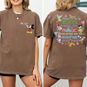 May include: Espresso-colored t-shirt featuring Mickey Mouse with a water gun and the text "Ma. Lact" on the front. The back of the shirt has a colorful graphic with Disney characters and the text "Welcome to School Where the Magic Never Stops and the Adventure Never Ends!"