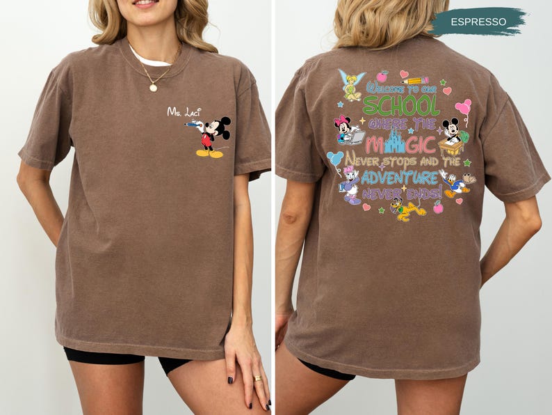 May include: Espresso-colored t-shirt featuring Mickey Mouse with a water gun and the text "Ma. Lact" on the front. The back of the shirt has a colorful graphic with Disney characters and the text "Welcome to School Where the Magic Never Stops and the Adventure Never Ends!"