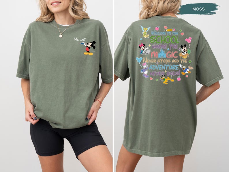 May include: Moss green t-shirt featuring Mickey Mouse with a water gun on the front. The back of the shirt has a colorful graphic with Disney characters and the text "Welcome to the School Where the Magic Never Stops and the Adventure Never Ends!"
