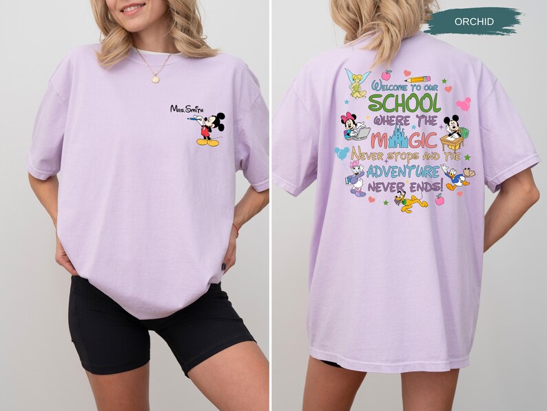 May include: Orchid-colored t-shirt featuring Mickey Mouse with a water gun on the front. The back of the shirt has a colorful graphic with Disney characters and the text "Welcome to our school where the magic never stops and the adventure never ends!"