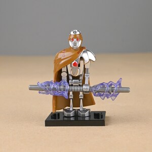 May include: A silver and brown action figure with a brown cape and a staff with purple energy effects. The figure is standing on a black base. The figure has a red eye.