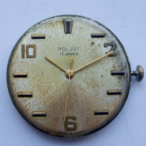 May include: Vintage Poljot watch face with gold hands and numerals. The watch face is a light beige color with the text "POLJOT 17 jewels" and "MADE IN USSR". The watch face has a crown and is slightly worn.
