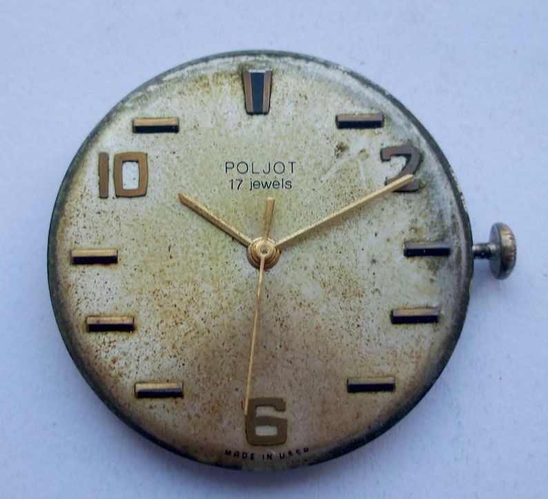 May include: Vintage Poljot watch face with gold hands and numerals. The watch face is a light beige color with the text "POLJOT 17 jewels" and "MADE IN USSR". The watch face has a crown and is slightly worn.