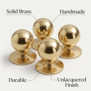 May include: Four solid brass, handmade door knobs with an unlacquered finish. The knobs are round with a polished, reflective surface. The image includes the words "Solid Brass", "Handmade", "Durable", and "Unlacquered Finish".