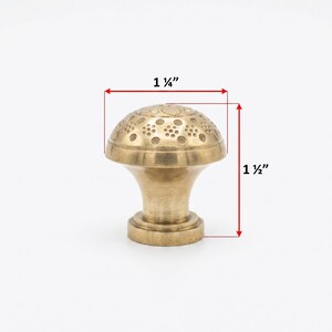 Puede incluir: Un tirador de armario de lat&oacute;n con un dise&ntilde;o floral decorativo en la parte superior. El tirador mide 3,18 cm de ancho y 3,81 cm de alto. El tirador tiene un dise&ntilde;o cl&aacute;sico y vintage.