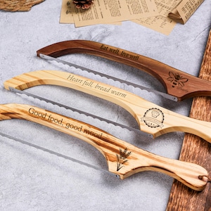 May include: Three wooden bread knives with serrated blades. The handles are engraved with phrases: "Eat well, live well", "Heart full, bread warm", and "Good food, good mood". One handle features a bee design, another a bakery logo, and the third a wheat design.