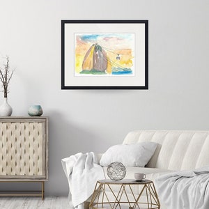 Puede incluir: Pintura acuarela de la monta&ntilde;a Pan de Az&uacute;car en R&iacute;o de Janeiro, Brasil. La monta&ntilde;a est&aacute; representada en tonos de marr&oacute;n, amarillo y naranja, con un telef&eacute;rico que asciende la monta&ntilde;a. El cielo es de un azul suave con nubes rosadas y naranjas.