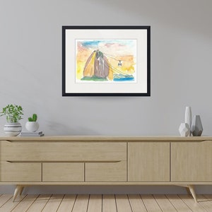 Puede incluir: Una pintura de acuarela de una monta&ntilde;a con un telef&eacute;rico que sube por el lado. La monta&ntilde;a est&aacute; pintada en tonos de marr&oacute;n, amarillo y naranja. El cielo est&aacute; pintado en tonos de azul y rosa. La pintura est&aacute; enmarcada en negro.
