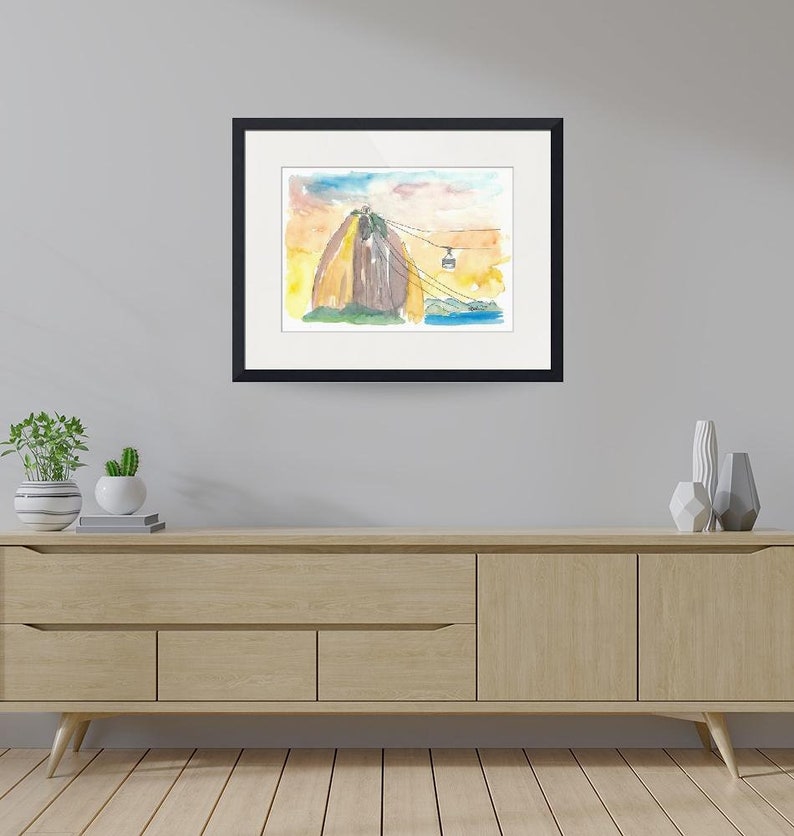 Puede incluir: Una pintura de acuarela de una monta&ntilde;a con un telef&eacute;rico que sube por el lado. La monta&ntilde;a est&aacute; pintada en tonos de marr&oacute;n, amarillo y naranja. El cielo est&aacute; pintado en tonos de azul y rosa. La pintura est&aacute; enmarcada en negro.