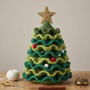 May include: A handmade crochet Christmas tree in shades of green, adorned with red and white baubles and gold star accents. The tree is topped with a gold star and sits on a wooden surface. A ball of white yarn and scissors are in the foreground.