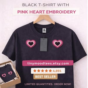 May include: Black t-shirt with pink heart embroidery. The shirt features two embroidered pink hearts. The text "tinymoodtees.etsy.com" is displayed, along with a best seller badge and a customer rating.