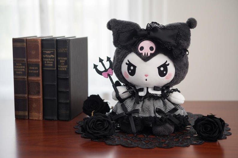 May include: A plush doll with a black and white checkered dress, black bow, and a skull on its head. It holds a trident with a pink bow. Black roses and books are in the background. The doll is approximately 8 inches tall.