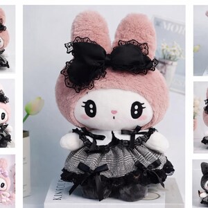 May include: A plush bunny doll with a pink hood and black bow. The doll wears a black and gray dress with lace trim. The bunny has large, expressive eyes and a small pink nose. The overall aesthetic is a blend of cute and gothic.