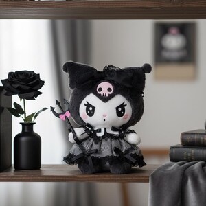 May include: A plush doll with a black and white color scheme, featuring a skull on its head and holding a trident. The doll is dressed in a black and gray dress. A black rose in a black vase is on the shelf.