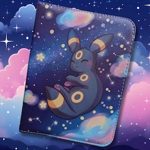 Può includere: Una copertina per taccuino rettangolare con uno sfondo di cielo notturno stellato blu scuro, nuvole color pastello e un'illustrazione centrale di una creatura dal pelo scuro con anelli gialli su orecchie, fronte e corpo in posa raggomitolata.