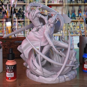 May include: An unpainted resin figurine showing two figures in a battle scene. One figure is armored and wielding a sword. Paint bottles and brushes are visible in the background. The figurine is ready for painting.