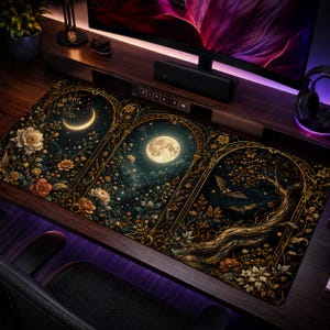 Puede incluir: Una alfombrilla de escritorio rectangular con un diseño de tres paneles y bordes de filigrana dorada. Los paneles muestran una luna creciente, una luna llena y un árbol oscuro con murciélagos, rodeados de motivos florales en tonos dorados.