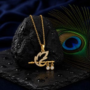 May include: A gold-toned pendant necklace featuring a stylised feather design encrusted with small clear stones, attached to a horizontal flute-shaped bar with two dangling circular charms, each set with a single clear stone on a fine chain.