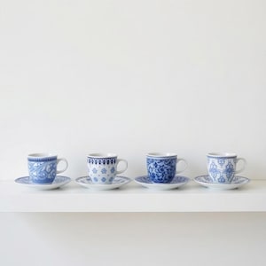 Peut inclure: Quatre tasses et soucoupes en porcelaine bleues et blanches assorties. Chaque tasse et soucoupe présente un motif floral et volute différent. Les tasses sont exposées sur une étagère blanche sur fond blanc.
