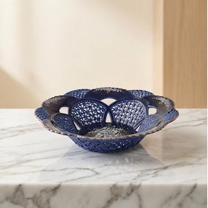 Peut inclure: Un bol en céramique bleu marine avec un motif ajouré. Le bol a un bord festonné avec une bordure dorée. Le motif en treillis complexe laisse passer la lumière, créant une esthétique délicate. Ce bol décoratif est idéal pour présenter des fruits ou comme centre de table.