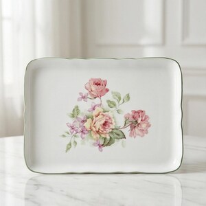 Peut inclure: Un plat de service rectangulaire en céramique blanche avec un bord festonné et une bordure verte. Le plat présente un motif floral de roses roses et jaunes avec des feuilles vertes et des accents violets.