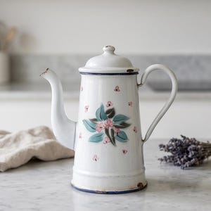Peut inclure: Une cafetière en émail blanc ornée d'un motif floral peint avec des feuilles bleu sarcelle et de petites fleurs roses. La cafetière possède un couvercle assorti, une anse courbée, un bec verseur et un fin liseré bleu sur la base et le couvercle.