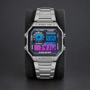 May include: A silver-tone digital wristwatch with a stainless steel link band. The square face features a black bezel, a world time map display, and a purple digital screen showing the time 7:41 and date 3-28. Text includes Casio, World Time, and Illuminator.