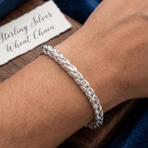 May include: A silver wheat chain bracelet. The bracelet has a woven design and is a bright silver colour. The text "Sterling Silver Wheat Chain" is on a white card in the background.