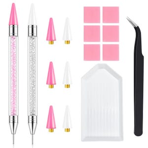 May include: A diamond painting tool set including two pens with clear barrels filled with pink and clear crystals, six interchangeable conical tips in pink and white, six pink wax squares, a white grooved tray, and black curved tweezers.
