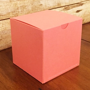 May include: A coral pink square gift box with a fold-over top. The box is sitting on a wooden surface. etsy.com/shop/annieslittleboxes