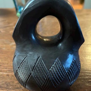 May include: A white ceramic mug with a black handle and the text "But First, Coffee" in a bold, black font. The mug is set against a blurred background, suggesting a cozy setting. The mug appears to be approximately 4 inches tall.