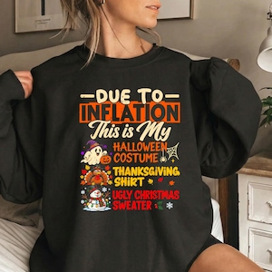 Może przedstawiać: Czarna bluza z długim rękawem z napisem "DUE TO INFLATION This is My HALLOWEEN COSTUME THANKSGIVING SHIRT UGLY CHRISTMAS SWEATER" oraz kolorowymi grafikami ducha z dynią, indyka i bałwana z lampkami świątecznymi.
