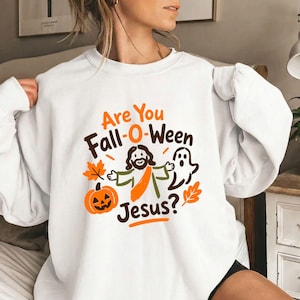 May include: A white crewneck sweatshirt featuring a graphic print with the orange and brown text Are You Fall-O-Ween Jesus? The design includes a cartoon figure of Jesus, a jack-o'-lantern pumpkin, a ghost, and two autumn leaves in orange and brown.