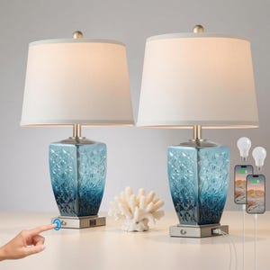 May include: A pair of table lamps with off-white drum shades and square, blue glass bases featuring a geometric, faceted pattern. Each lamp base includes a metallic silver square stand with a built-in USB port and a touch-sensitive power button.