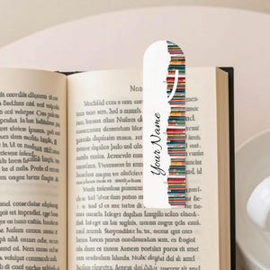 May include: An open book with a white bookmark featuring a colourful stack of books design. The bookmark has the text "Your Name". A cup of coffee is placed on a table nearby.