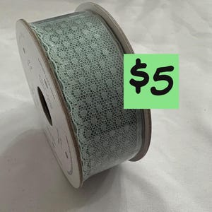 May include: A spool of light green lace trim. The lace has a delicate, openwork pattern. The spool is made of cardboard and has a label. A green square with the number 5 in black is visible.