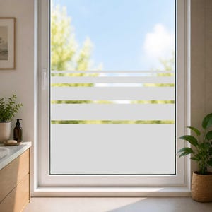Könnte beinhalten: Ein weißes Fenster mit horizontalen, mattierten Streifen. Das Fenster ist in einem weißen Rahmen eingefasst und bietet einen Blick auf einen strahlend blauen Himmel und grünes Laub. Das Fenster befindet sich in einem Badezimmer.