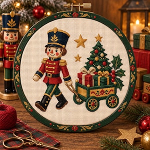 Könnte beinhalten: Ein runder Stickrahmen mit einem Kreuzstichmotiv eines Nussknackers in rot-blauer Uniform, der einen grünen Wagen mit verpackten Geschenken und einem geschmückten Weihnachtsbaum zieht, ergänzt durch zwei goldene Sterne auf cremefarbenem Stoff.