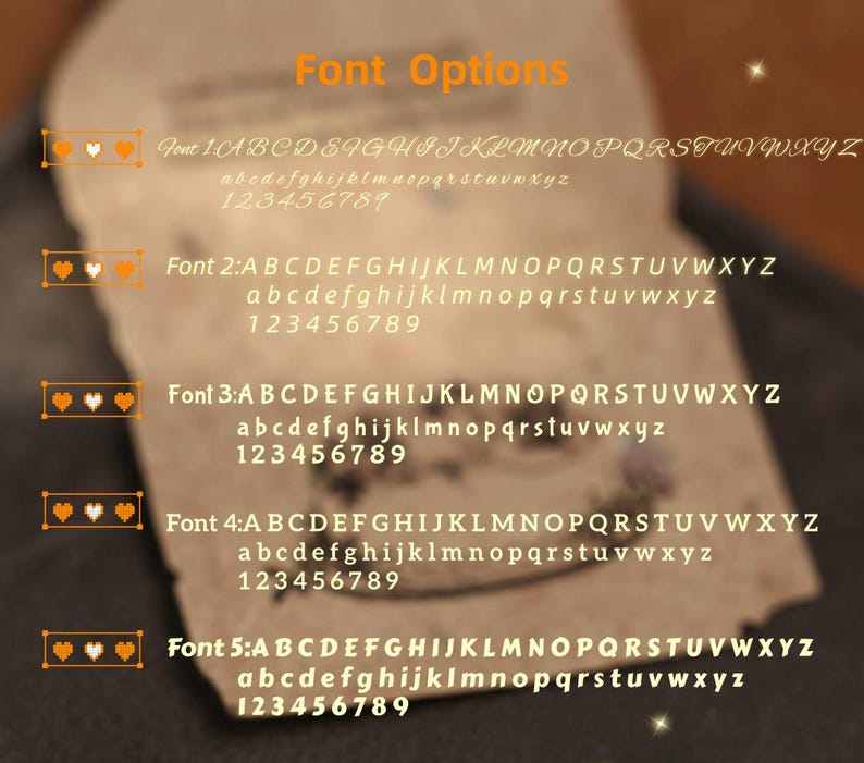 May include: A close-up of a paper with font options. The text "Font Options" is in orange. Five font styles are displayed, each with uppercase and lowercase alphabets and numbers. Each font is labeled with a number and a heart icon.
