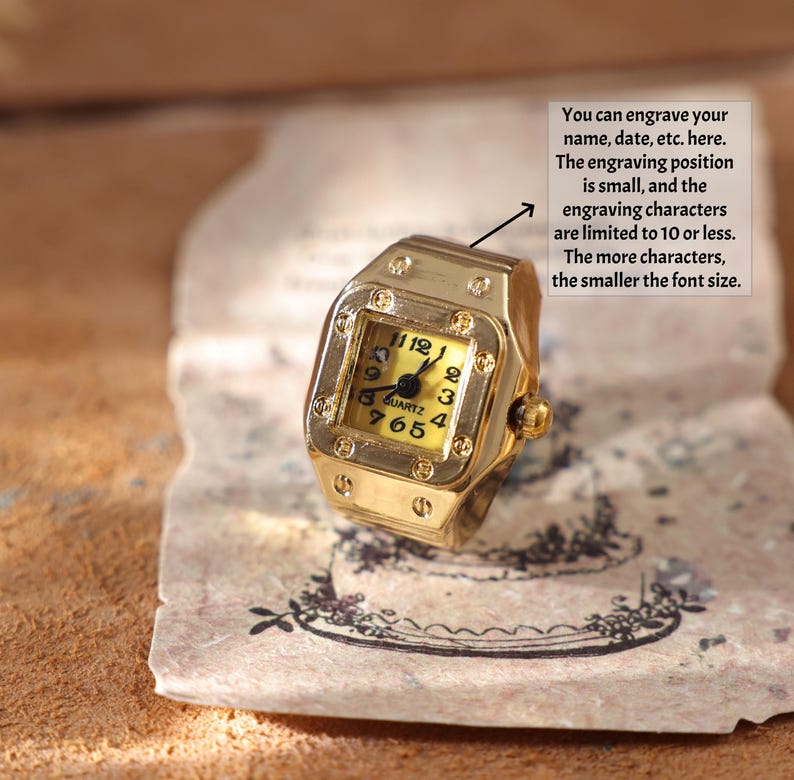 May include: A gold-colored ring shaped like a wristwatch, featuring a square face with black numerals on a yellow background. The ring has a quartz movement and the text "QUARTZ" is visible. The image includes text about engraving.
