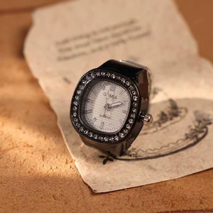 May include: A white ceramic mug with a black handle and the text "But First, Coffee" in a black, handwritten-style font. The mug is on a white surface.