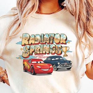 May include: A white ceramic mug with a black handle and the text "But First, Coffee" in a black, bold font. The mug is on a wooden surface.