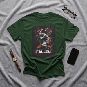Könnte beinhalten: Dunkelgrünes T-Shirt mit einer verblassten Grafik eines knienden Engels mit Heiligenschein und Flügeln. Das Wort "FALLEN" ist weiß unter dem Bild gedruckt. Eine braune Lederuhr, eine schwarze Brille und ein Smartphone sind ebenfalls sichtbar.