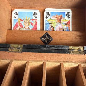 May include: Wooden box with playing cards featuring illustrations of royalty. The cards are arranged in a wooden compartment. The box has a hinged lid and a small, black and gold label that reads "FO BOXES".