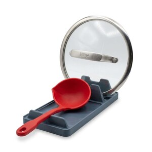 May include: A dark gray rectangular kitchen utensil rest holding a red ladle and a circular glass pot lid with a stainless steel rim and handle. The handle of the lid features the embossed text Ninja, providing a stable base for cooking tools.