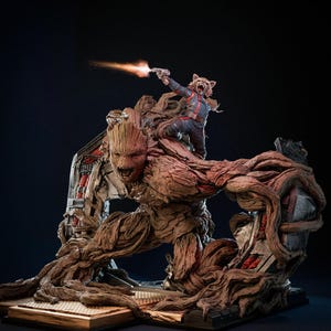 Könnte beinhalten: Eine detaillierte Statue mit Groot und Rocket aus Guardians of the Galaxy. Groot ist eine große, braune, baumartige Figur, auf deren Schulter Rocket, ein Waschbär, sitzt und eine Waffe abfeuert. Die Statue hat komplizierte Details und einen dunklen Hintergrund.