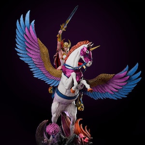 Puede incluir: Figura detallada de una guerrera montada en un unicornio alado. La guerrera viste una armadura dorada y roja, empuñando una espada en alto. El unicornio tiene un cuerpo blanco, detalles morados y rosas, y grandes alas con plumas azules, rosas y doradas. La base es un paisaje rocoso.