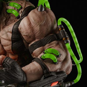 Op de afbeelding: Close-up van een gespierde figuur met een getextureerde huid. De figuur heeft zwarte banden en buizen gevuld met felgroene vloeistof. De figuur draagt zwarte handschoenen en heeft een mechanisch apparaat op de arm. De achtergrond is zwart.
