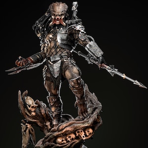 Puede incluir: Estatua detallada de Predator, con el cazador alienígena en una pose dinámica. La figura está vestida con una armadura intrincada y sostiene armas con cuchillas. La base es un tronco de árbol texturizado con calaveras.
