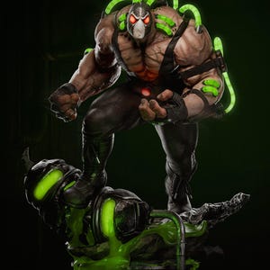 Op de afbeelding: Een gedetailleerd beeld van de DC Comics-schurk Bane, staand op een platform met groen oplichtende accenten. Bane wordt afgebeeld met een masker, buizen en een gespierd lichaam. Het beeld heeft een donker kleurenpalet met groene highlights.